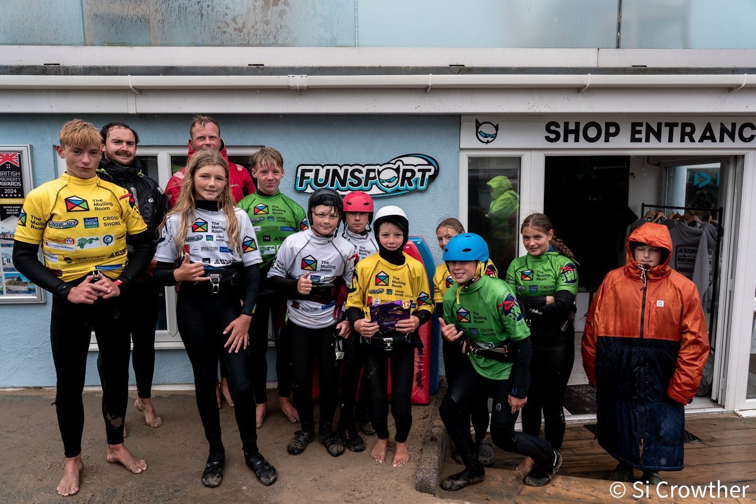 Young Future Pros riders in wetsuits and helmets outside the Rhosneigr windsurf shop